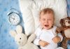 How to Handle Your Baby Crying at Night A baby crying at night with an alarm clock and teddy by his side
