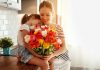 100 Lovely Mother’s Day Quotes & Wishes To Make Your Mom Feel Special A little girl giving a bouquet of flowers to her mother